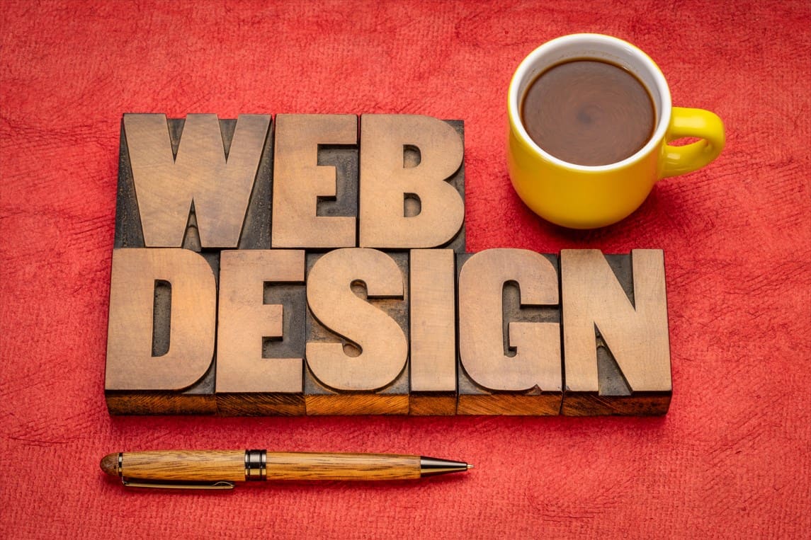 Creative web design setup with wooden letters, yellow mug, and a pen on a red background, illustrating Low Cost Printing's web design services.